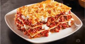A hearty slice of homemade lasagna served on a white plate, showing layers of pasta, rich meat sauce, creamy ricotta, and melted golden cheese