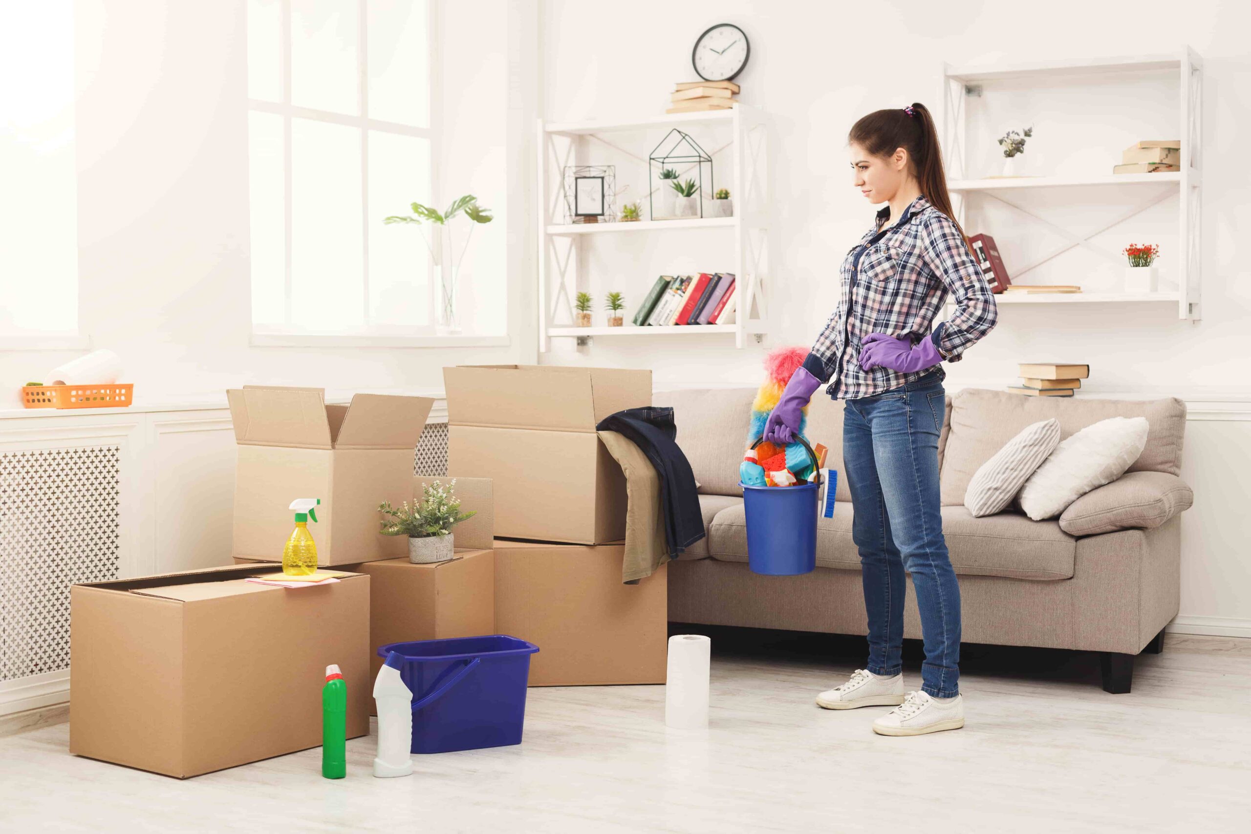 Woman preparing for Apartment Clean Out Services Kent WA with cleaning supplies and moving boxes in a bright living room.