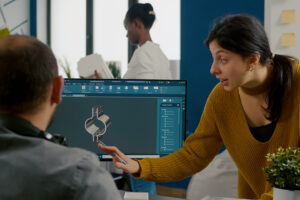 Female designer discussing a 3D CAD model with a colleague in an office.