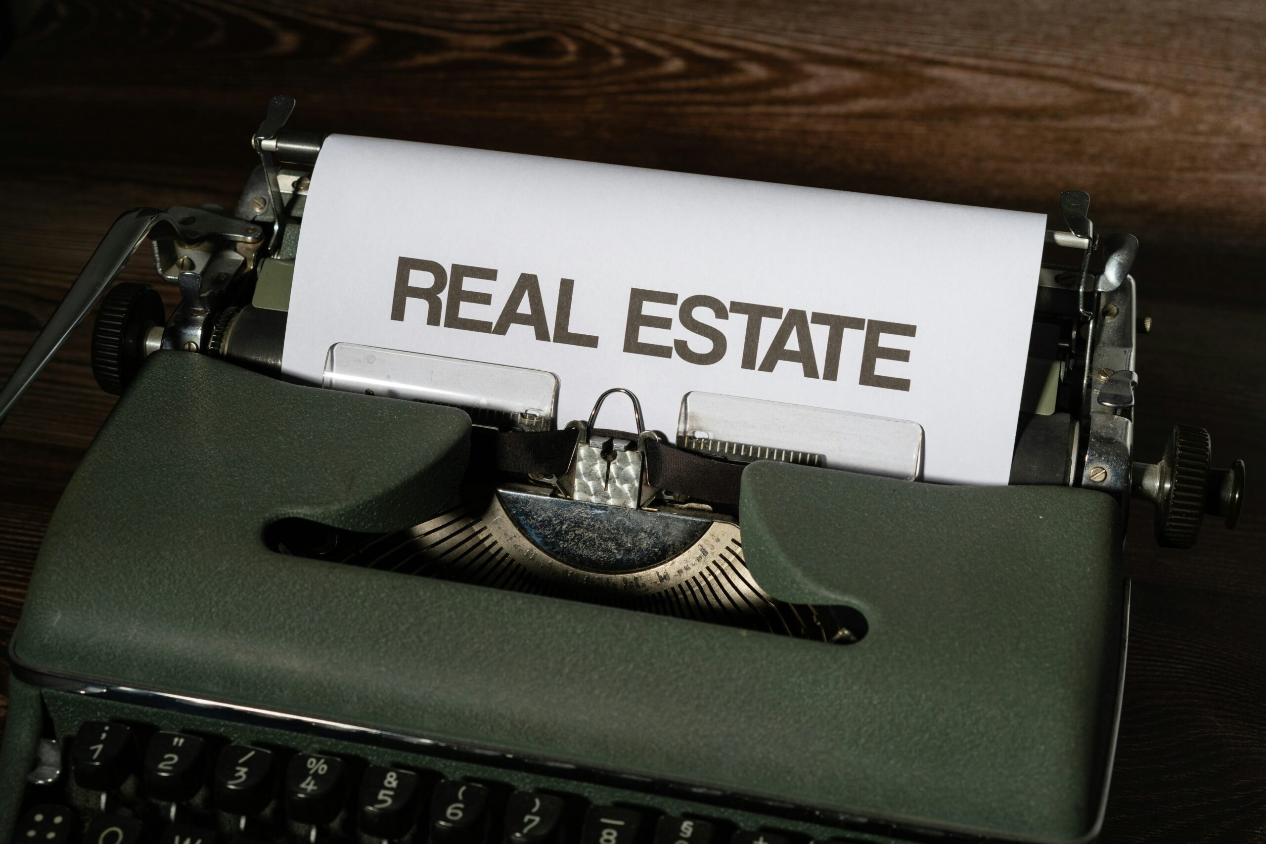 close-up of a vintage typewriter with a sheet of paper displaying the words "REAL ESTATE" in bold letter