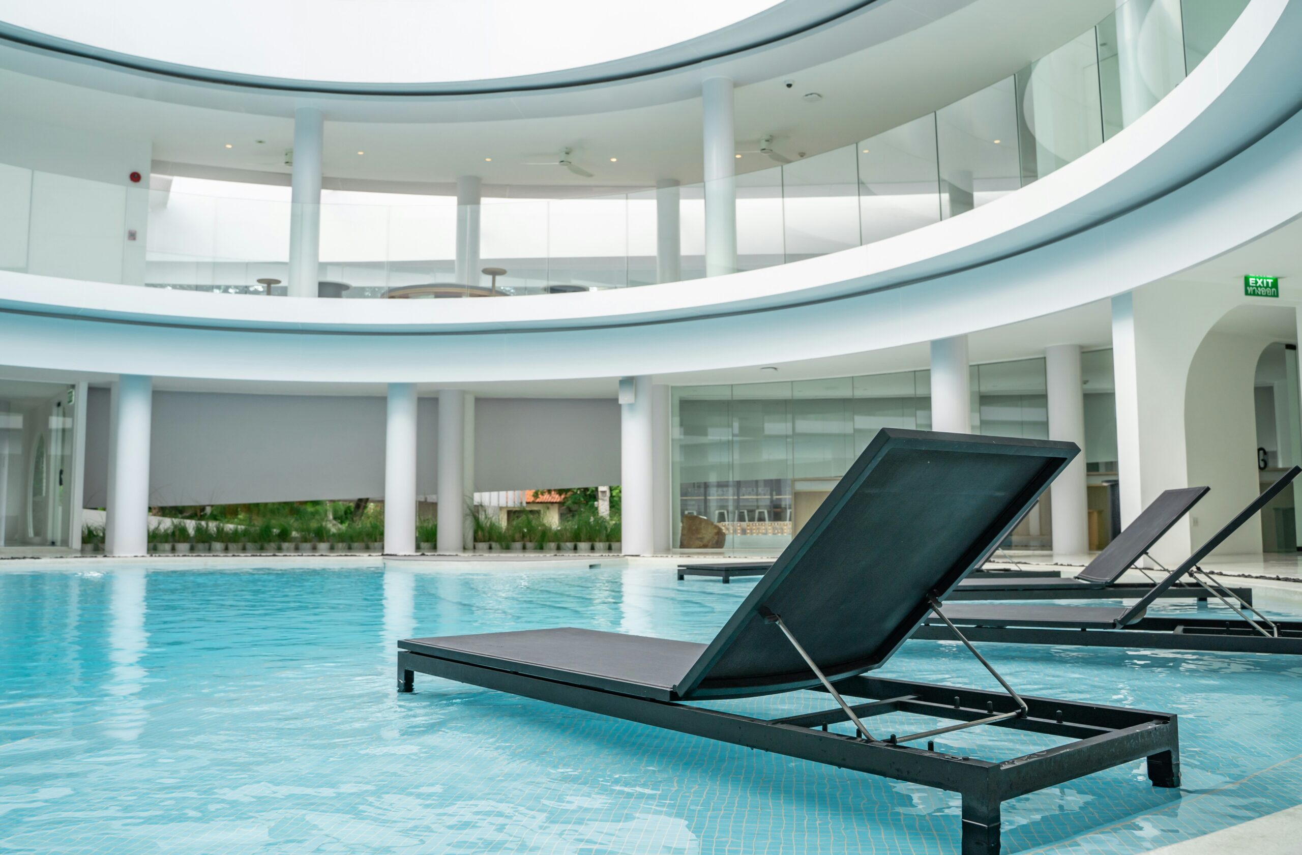 Modern luxury indoor pool area with sleek black lounge chairs and curved glass architecture.